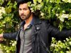Varun Dhawan Top Grossers
A man with dark hair and a beard wearing a black leather jacket poses among green foliage with white flowers in the background.