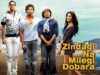 Zindagi Na Milegi Dobara–A Timeless Celebration of Life, Friendship & Fearless Living
A group of four young adults, three men and one woman, standing outdoors in front of houses and mountains, with a vintage car on the right, promoting the Indian film "Zindagi Na Milegi Dobara".
