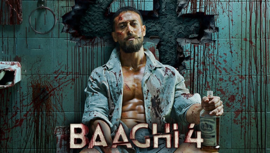 baaghi 4 feature Blood-splattered man sitting on a toilet with a knife and a bottle of alcohol in a gruesome, horror-themed setting from the movie "BACH 4".